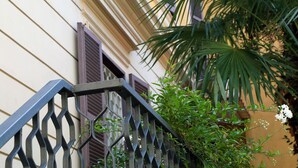 A building with a balcony, a window with shutters, and a plant with white flowers. - Roma Room Hotel (Rome)