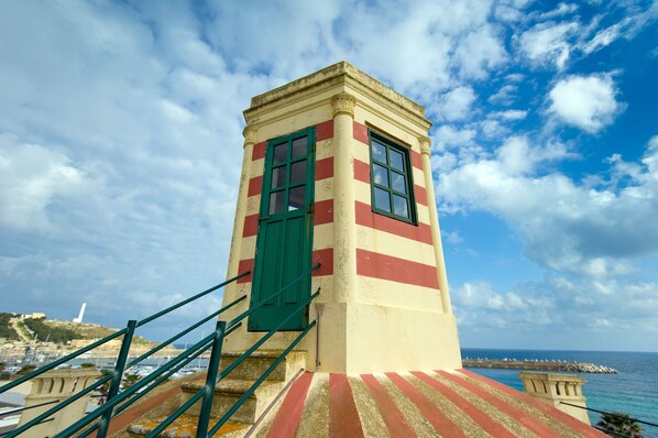 Un faro costero con fachada a rayas rojas y blancas, una puerta verde y una escalera que lleva a él.
