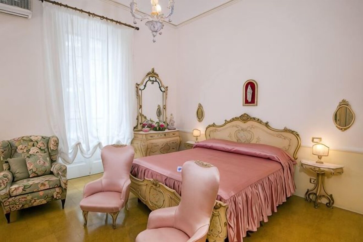 A bedroom with a bed, two chairs, a vanity, and a chandelier.