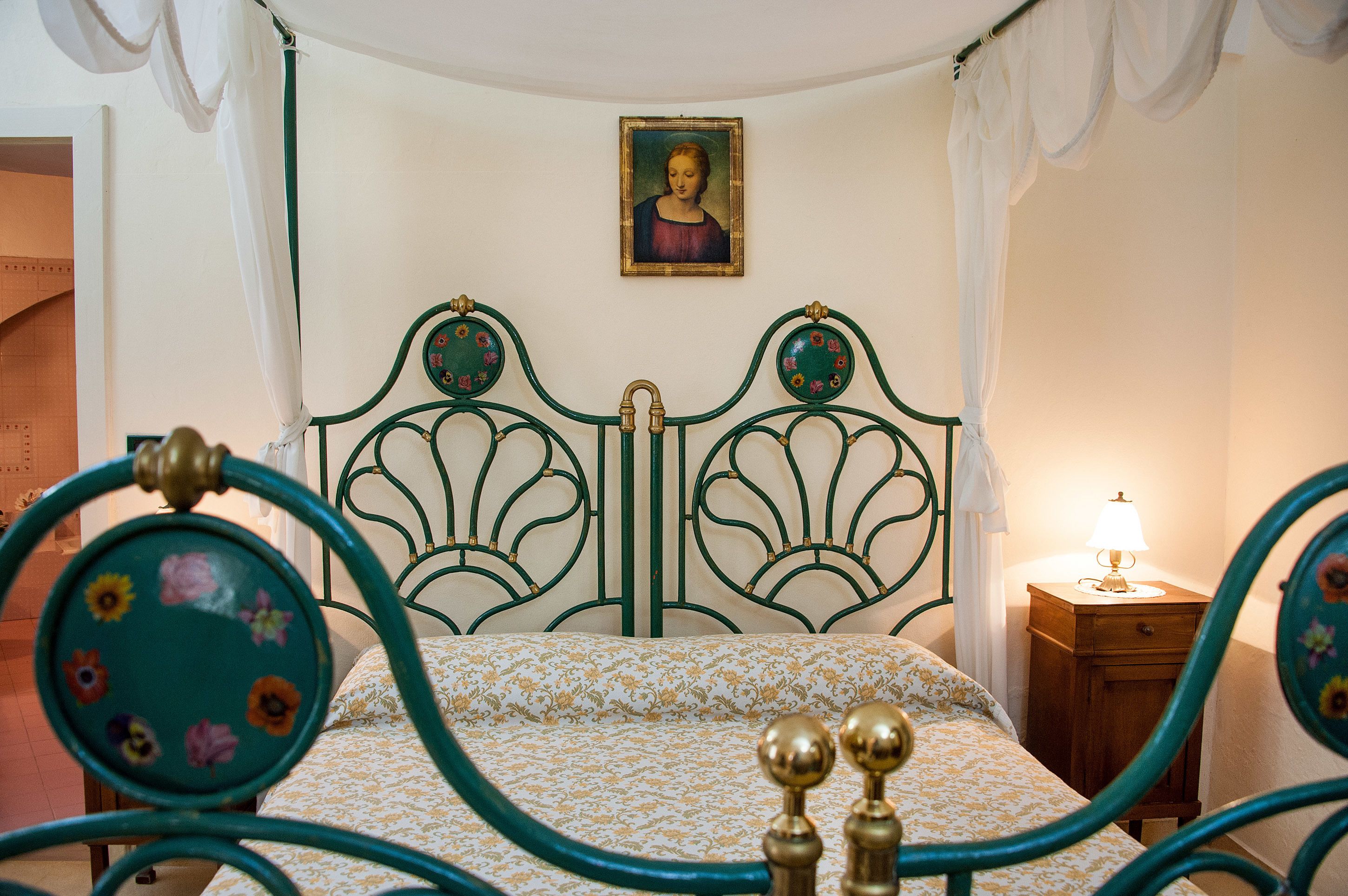Ein Bett mit einem blumigen Überwurf, ein Nachttisch mit einer Lampe und ein Bild an der Wand.
