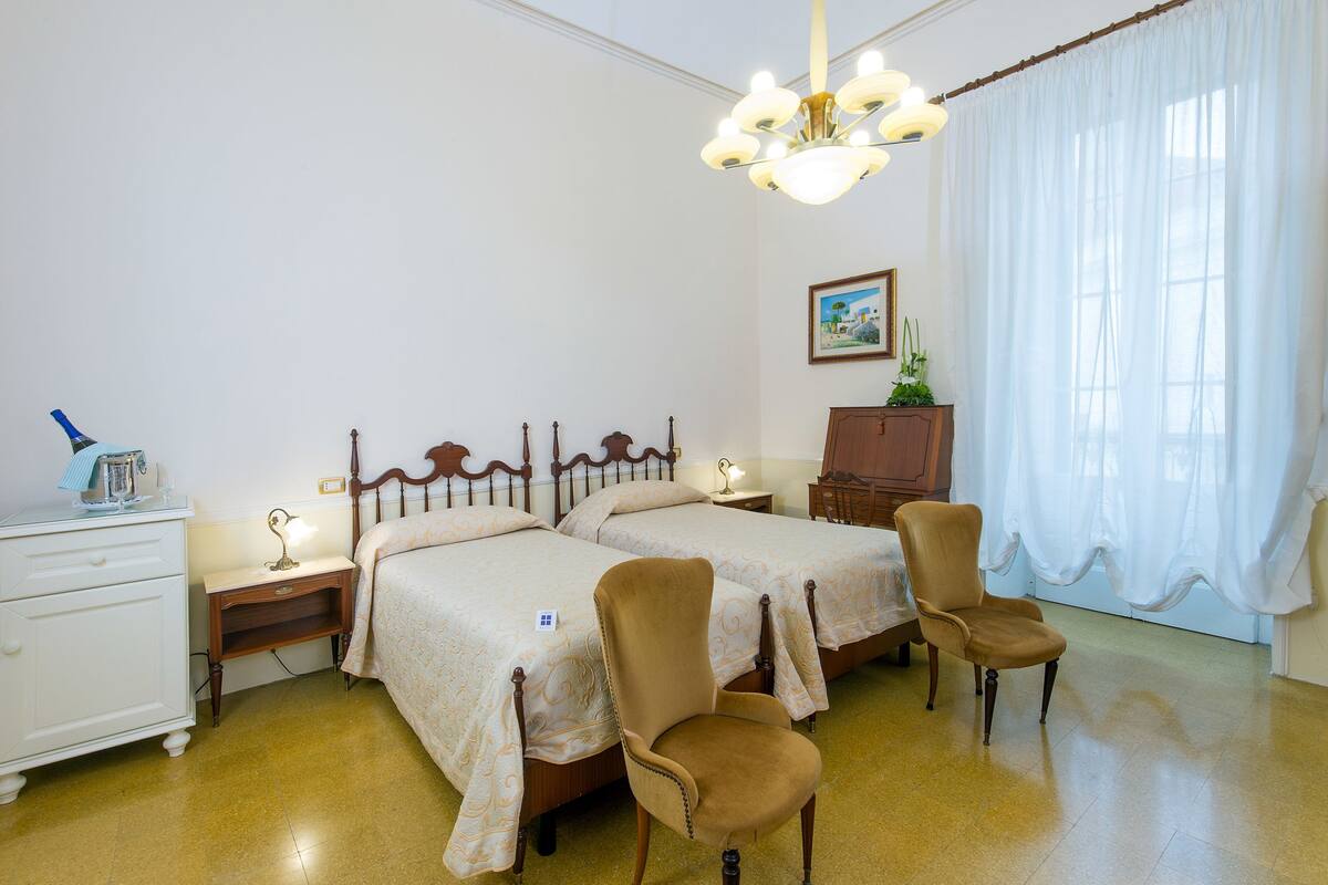 Un dormitorio con dos camas, una mesita de noche, un aparador, una silla y una araña.