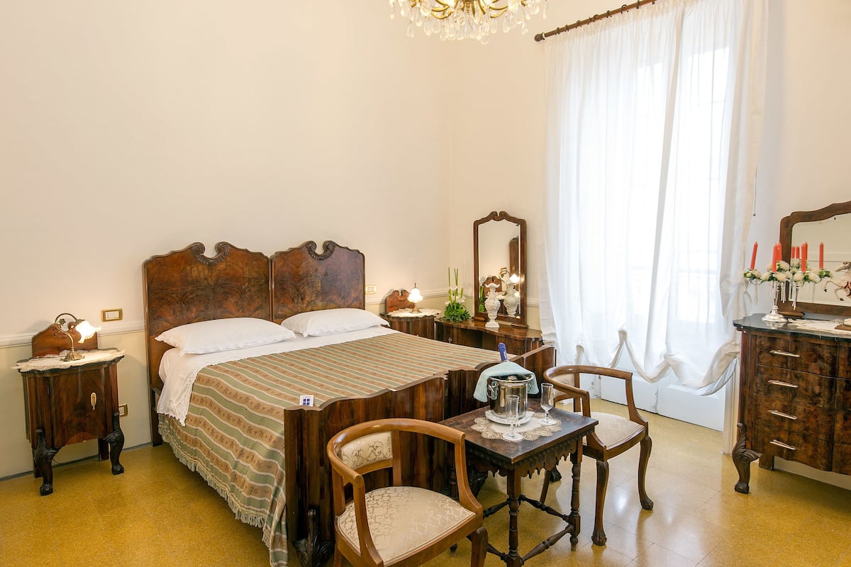 Un dormitorio tradicional con cama de madera, mesita de noche, cómoda y mesa con sillas.
