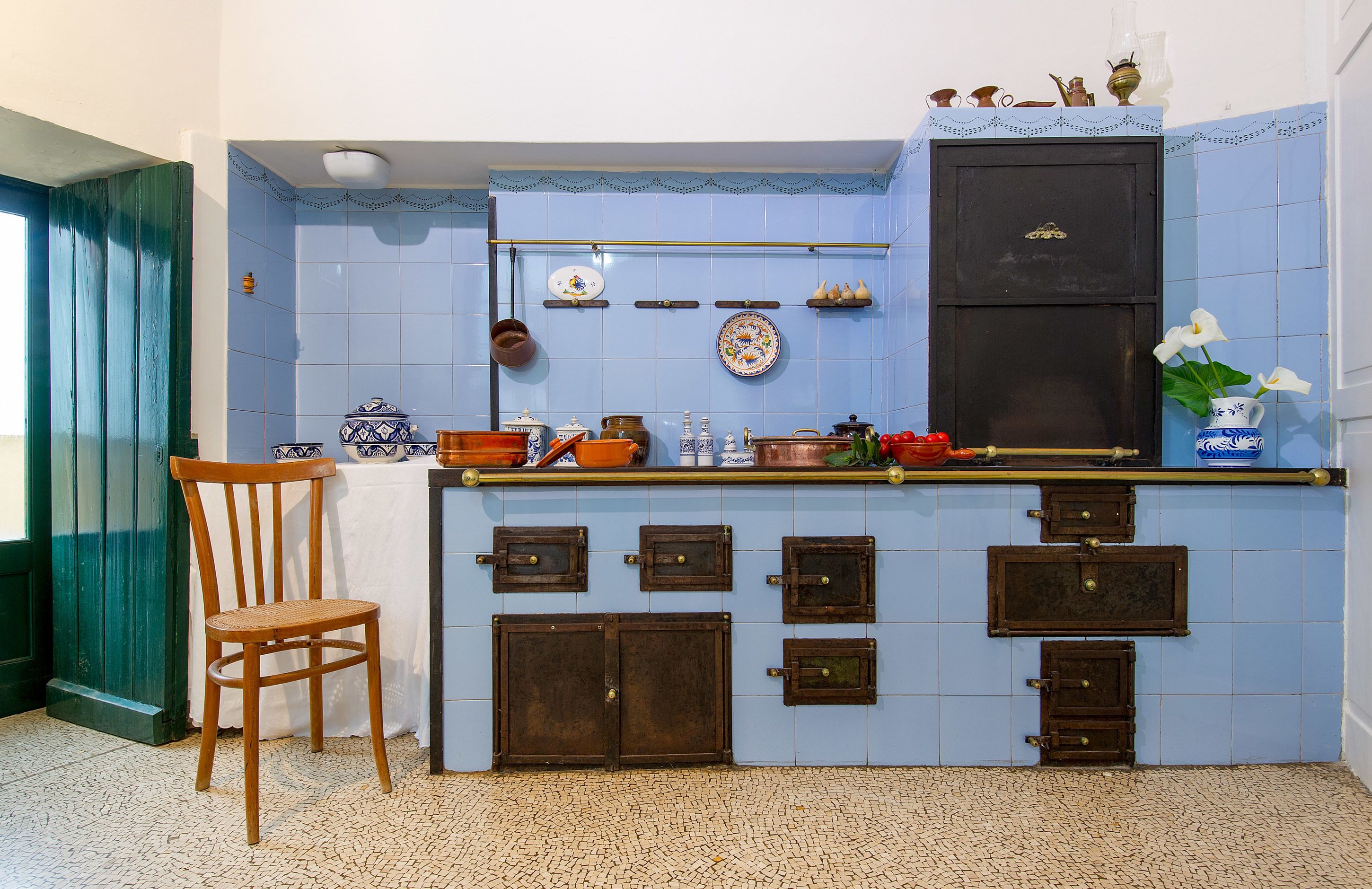A kitchen with blue tiles, wooden cabinets, and a chair.