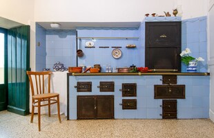 A kitchen with blue tiles, wooden cabinets, and a chair.