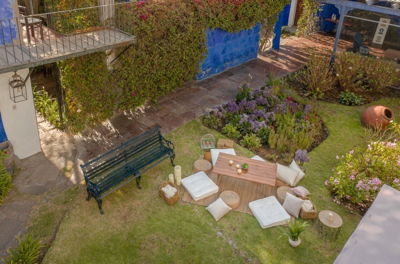 A garden patio with a wooden table, white cushions, and a bench.
