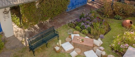 A garden patio with a wooden table, white cushions, and a bench.