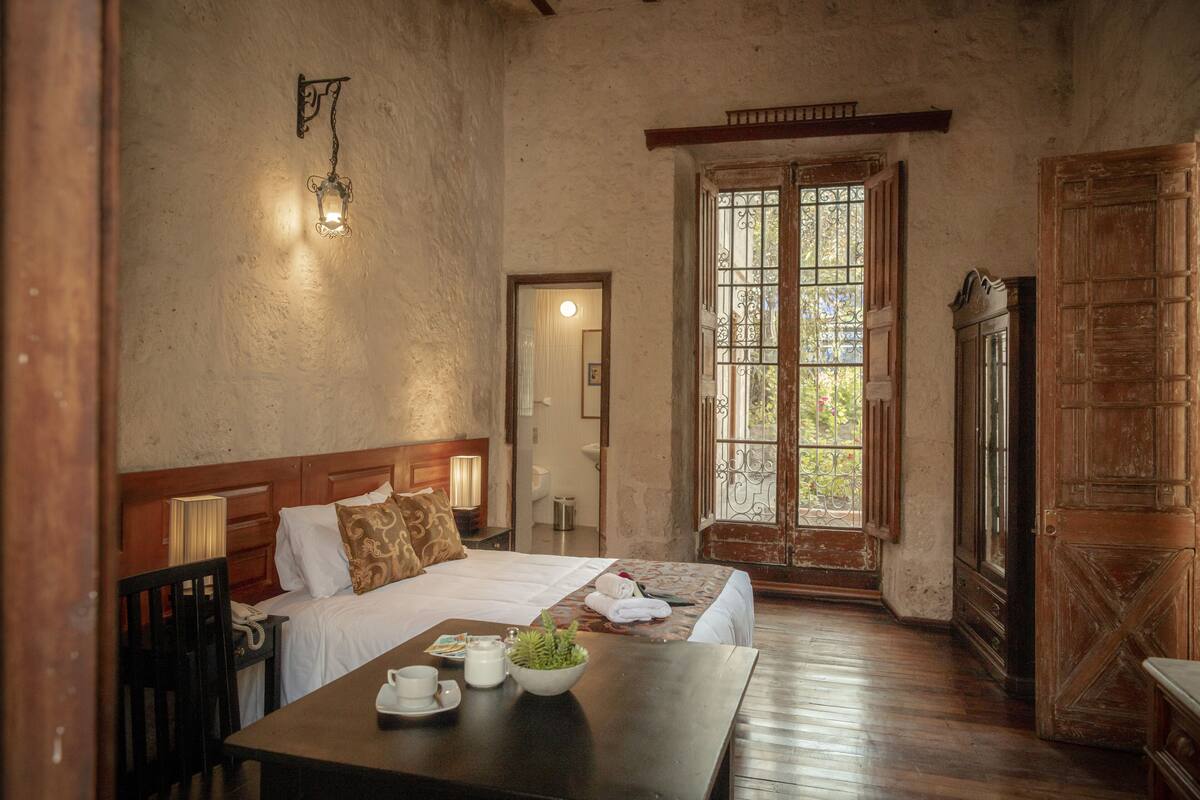 A room with a bed, bedside table, lamp, and a window with a view.