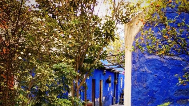 Un chemin de pierre mène à un bâtiment aux murs bleus et au toit recouvert de tuiles.
