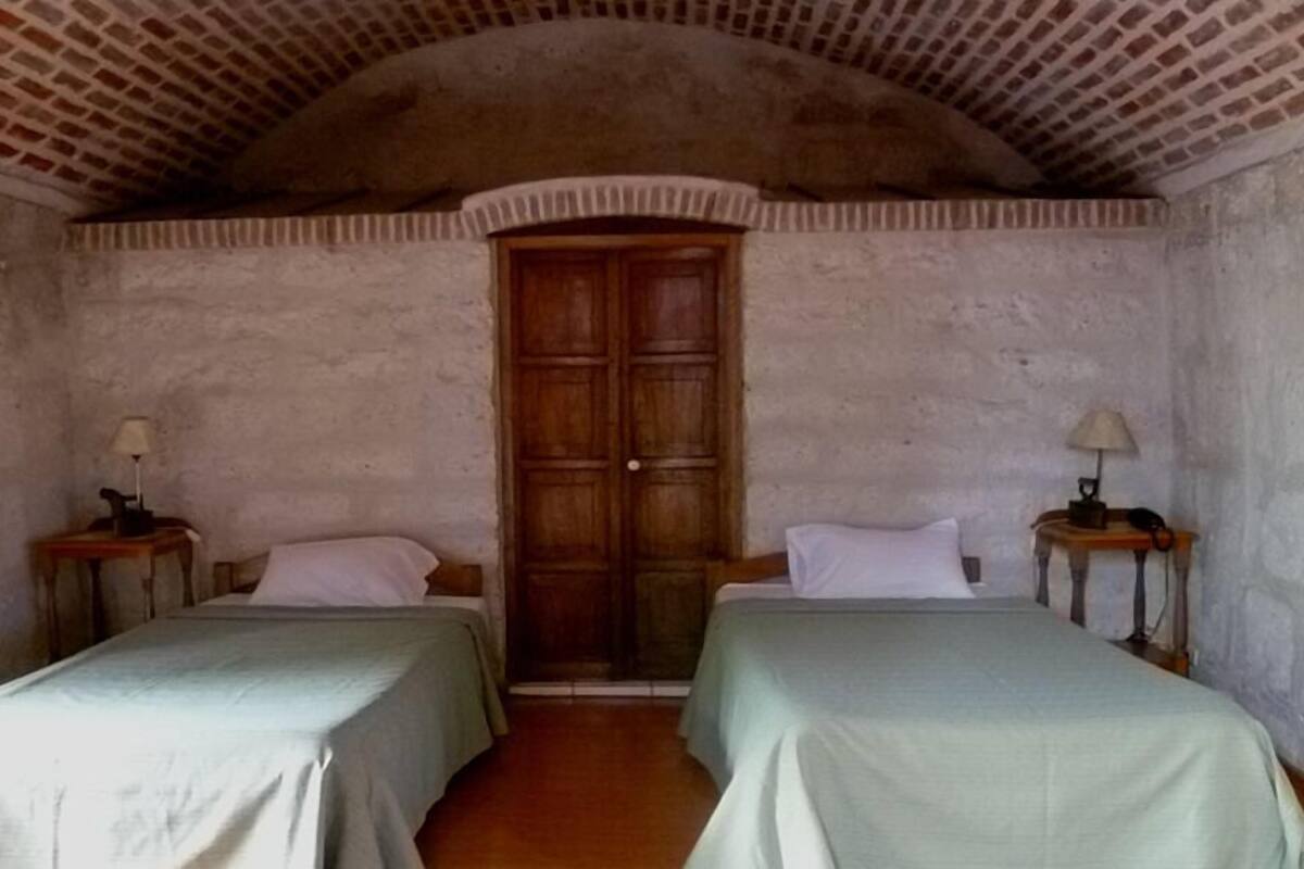 A room with two beds, a wooden door, and two bedside tables with lamps.