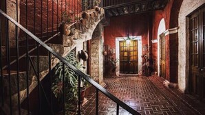 Un couloir étroit aux murs de briques, avec un escalier sur la gauche, menant à une porte dotée d’un panneau de verre.