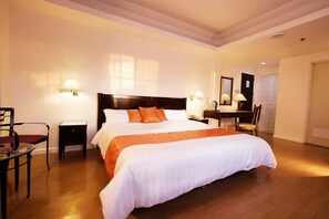 A hotel room with a large bed, two bedside tables, a desk with a chair, a mirror, and a wardrobe. - Harbor Town Hotel (Iloilo)
