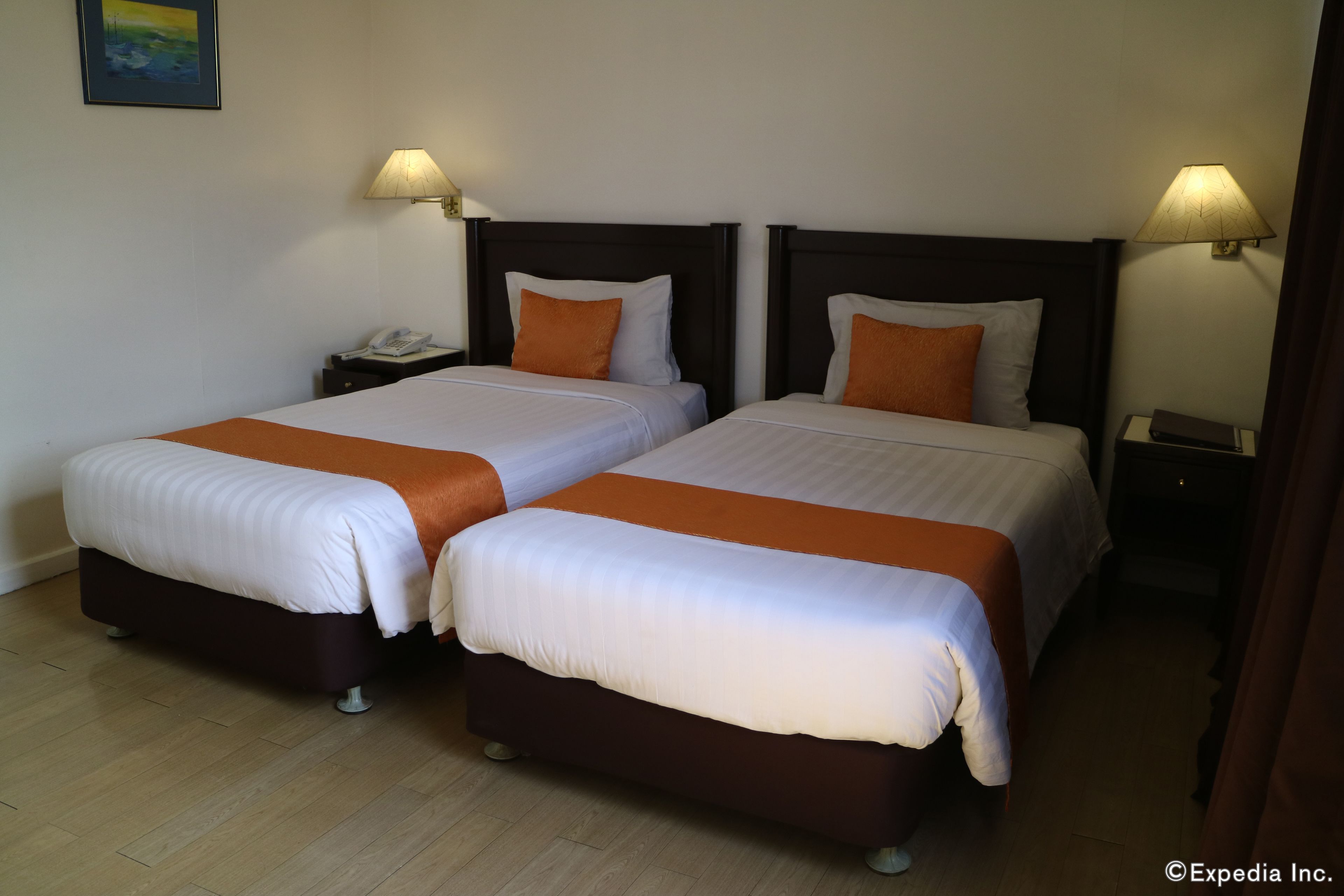 A hotel room with two beds, each with a wooden headboard and white bedding. There are two bedside lamps and a telephone on the nightstand.