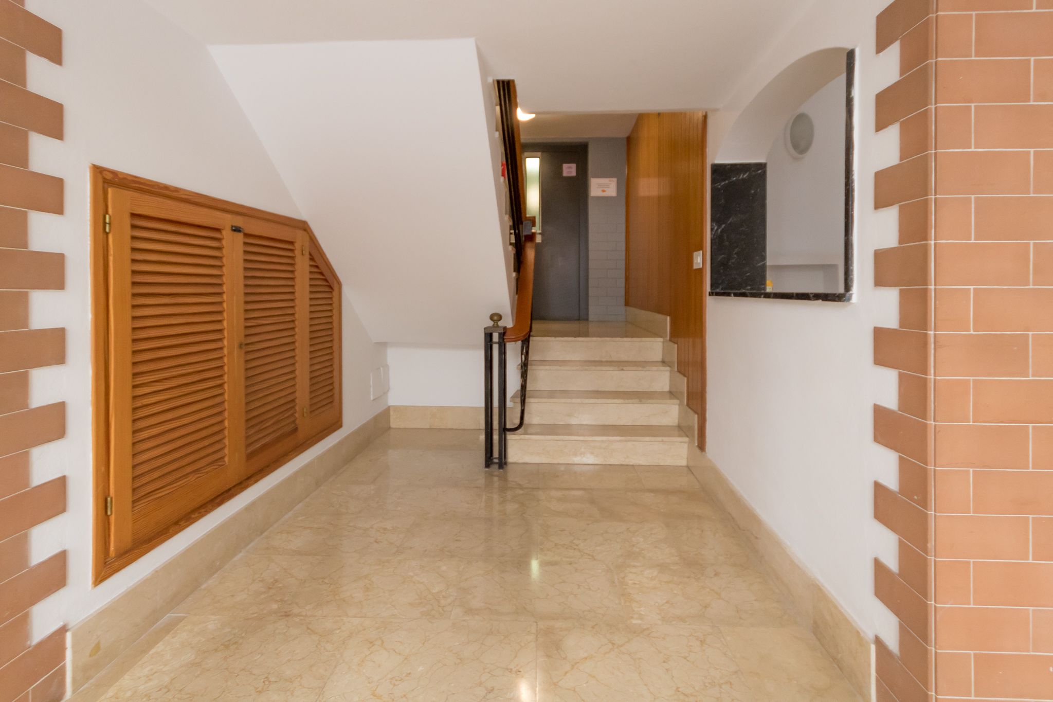Un passadís amb una porta de fusta, un sòl de marbre i una escala que porta a una altra habitació.