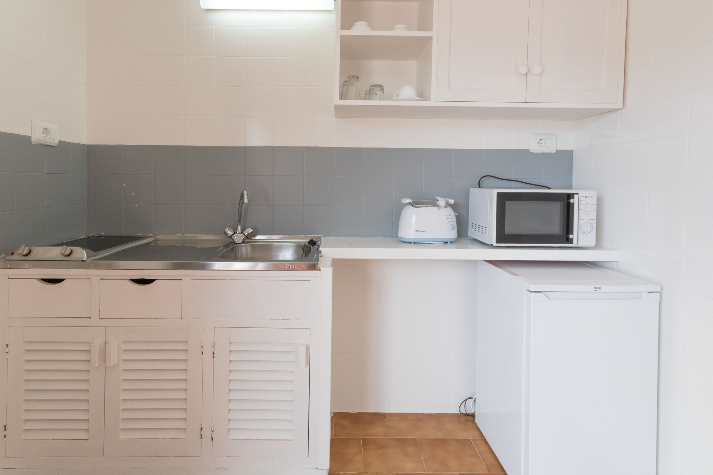 A compact kitchen with a sink, a toaster, a microwave, and a refrigerator.