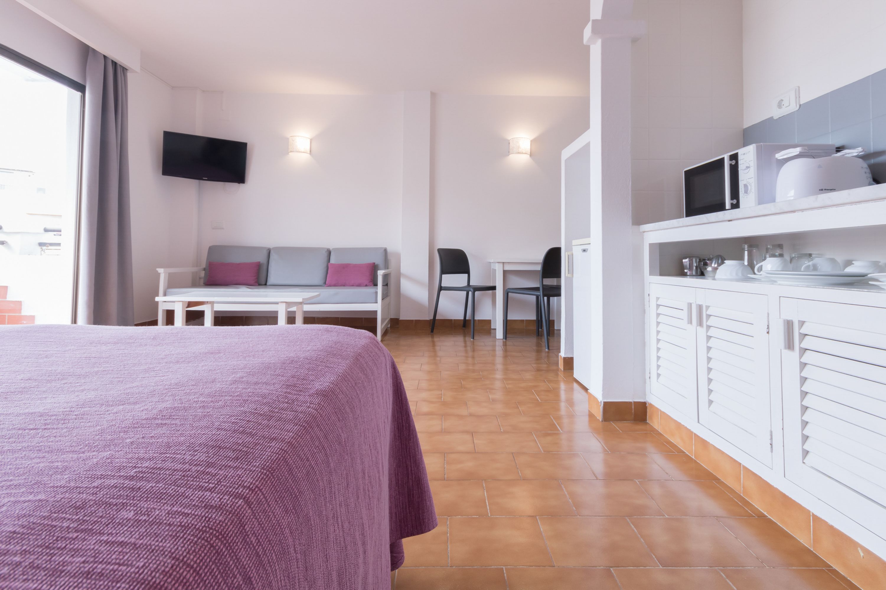 Habitación de hotel con cama, sofá, mesa de comedor y zona de cocina con armarios y microondas.