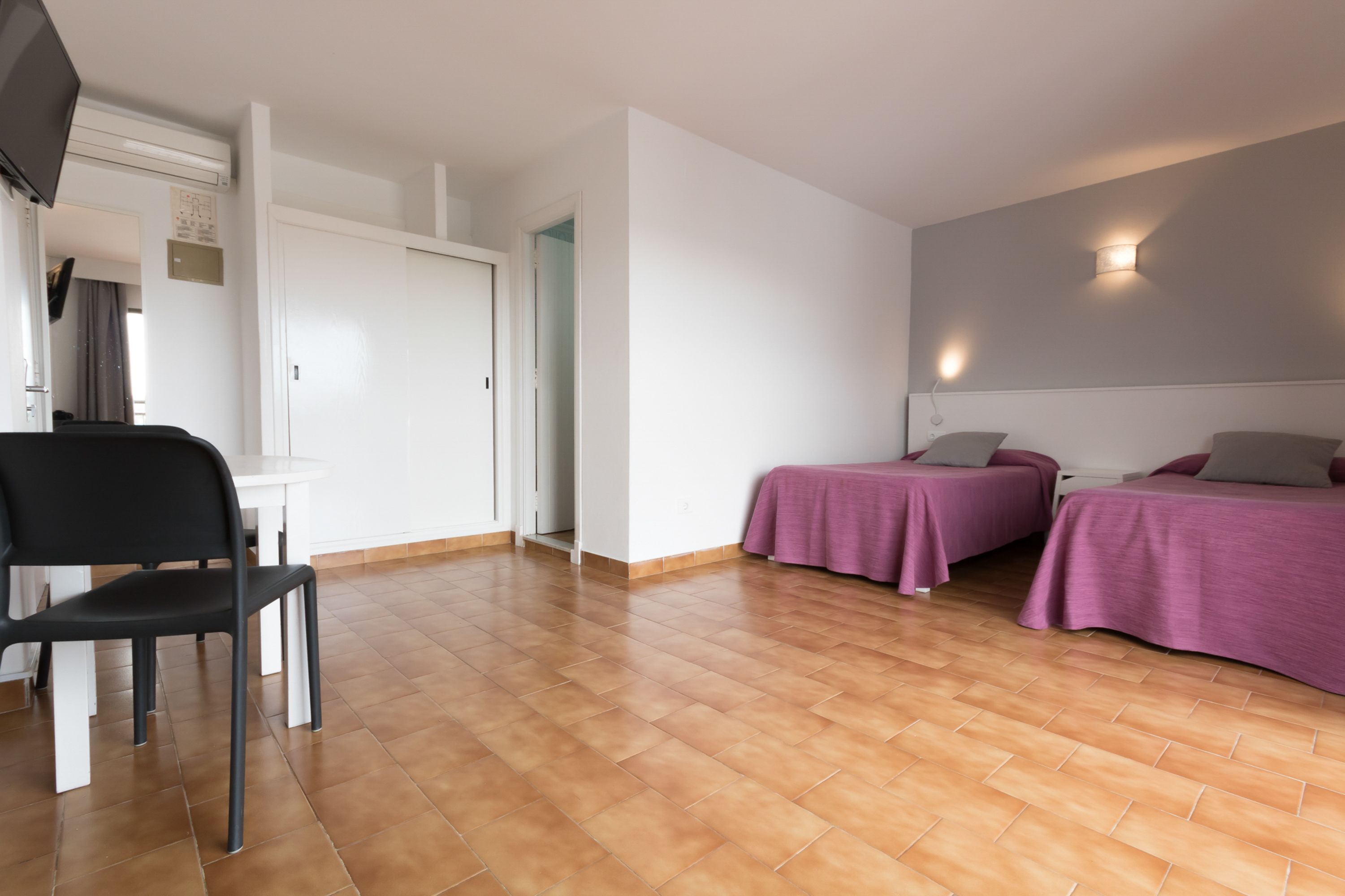 Ein Zimmer mit zwei Betten, einem Sessel, einem kleinen Tisch und einer weißen Tür.