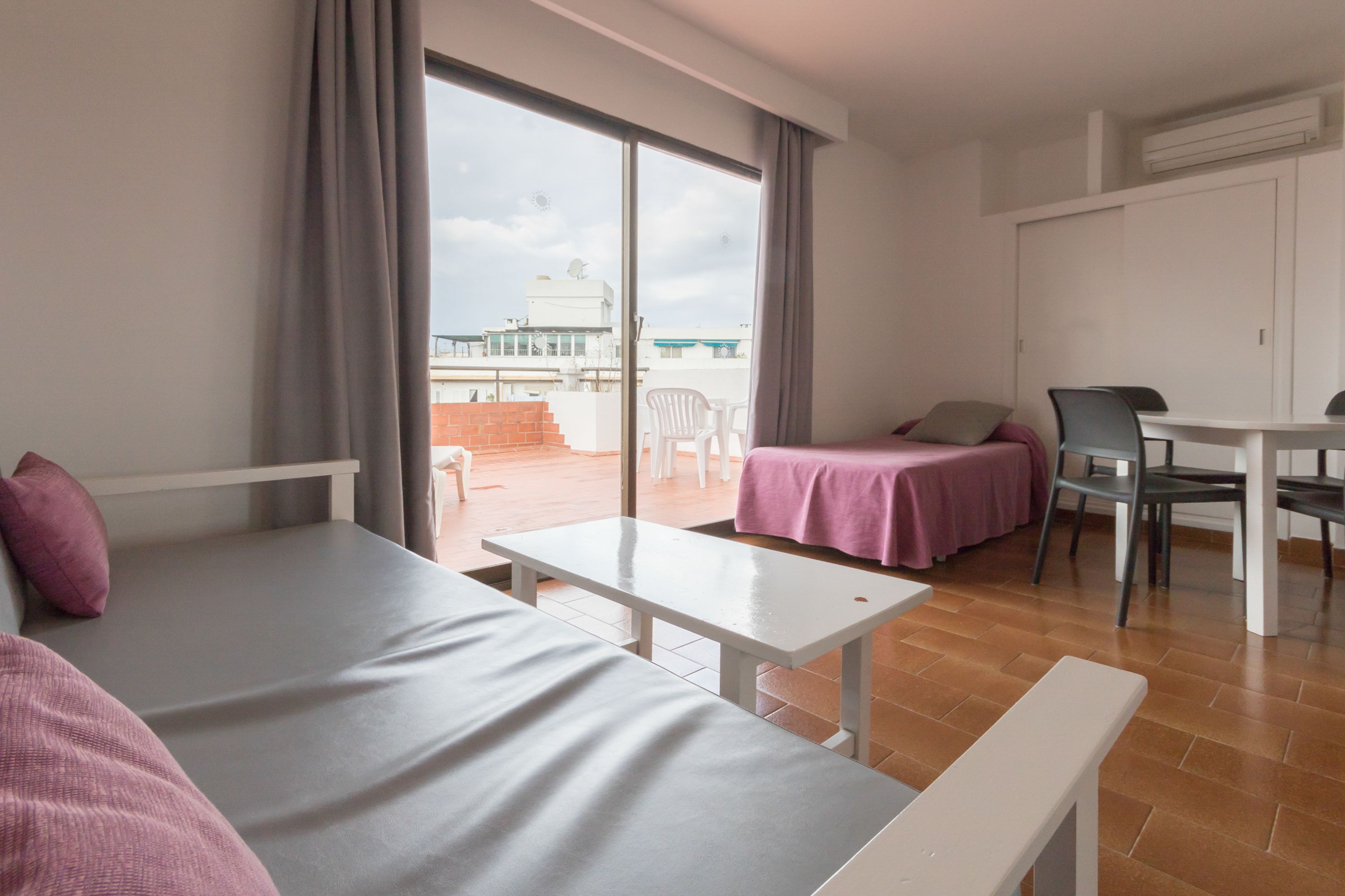 A room with a bed, a table, a chair, and a view of the outside.