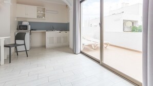 A modern kitchen with white cabinets, a microwave, and a sink. There's a dining area with a table and chairs. A large sliding glass door leads to an outdoor patio with a white table and chairs.