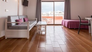 A modern hotel room with a balcony, a sofa, a small table, and a bed with a purple bedspread.