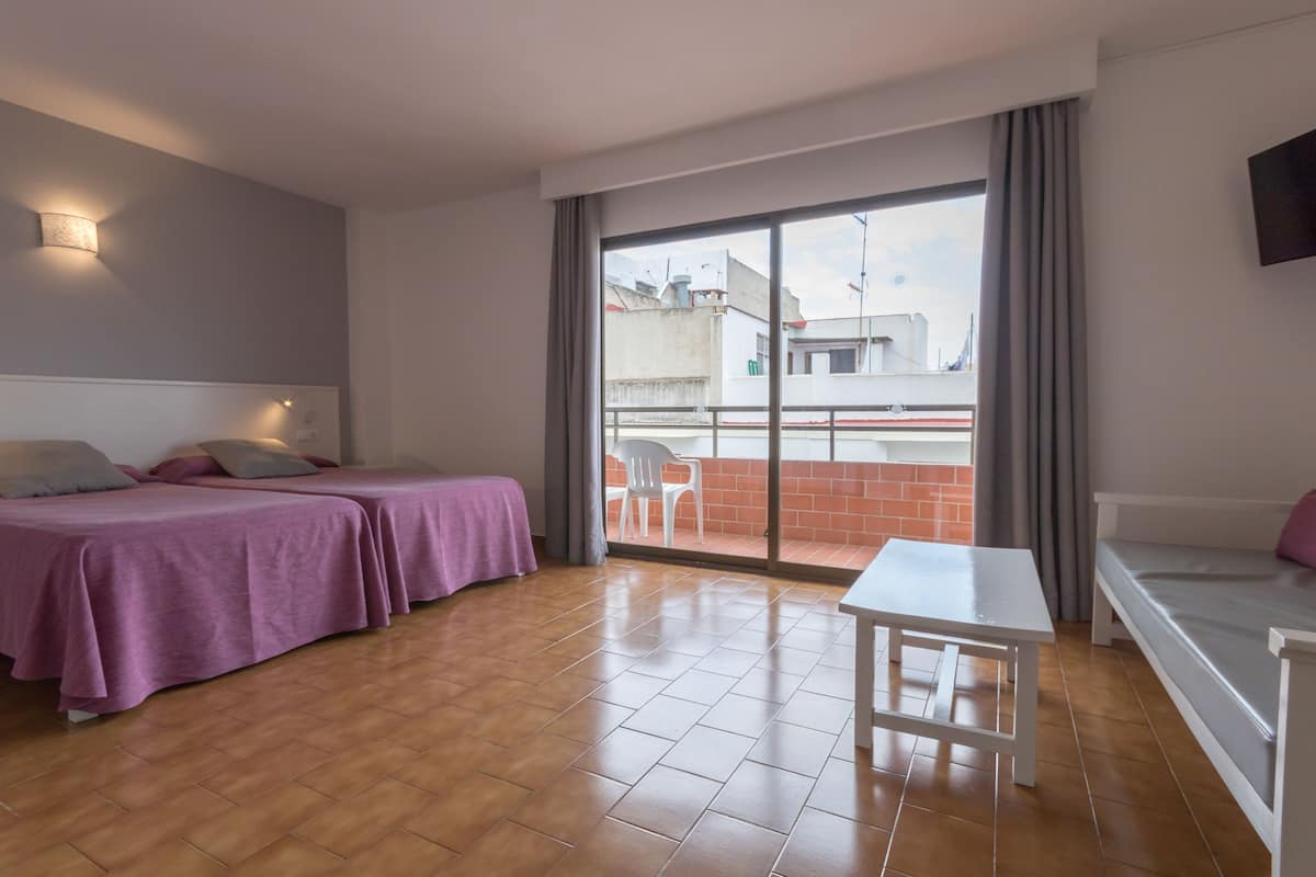 Una habitación con dos camas, una mesa blanca y vista a un balcón con una silla.