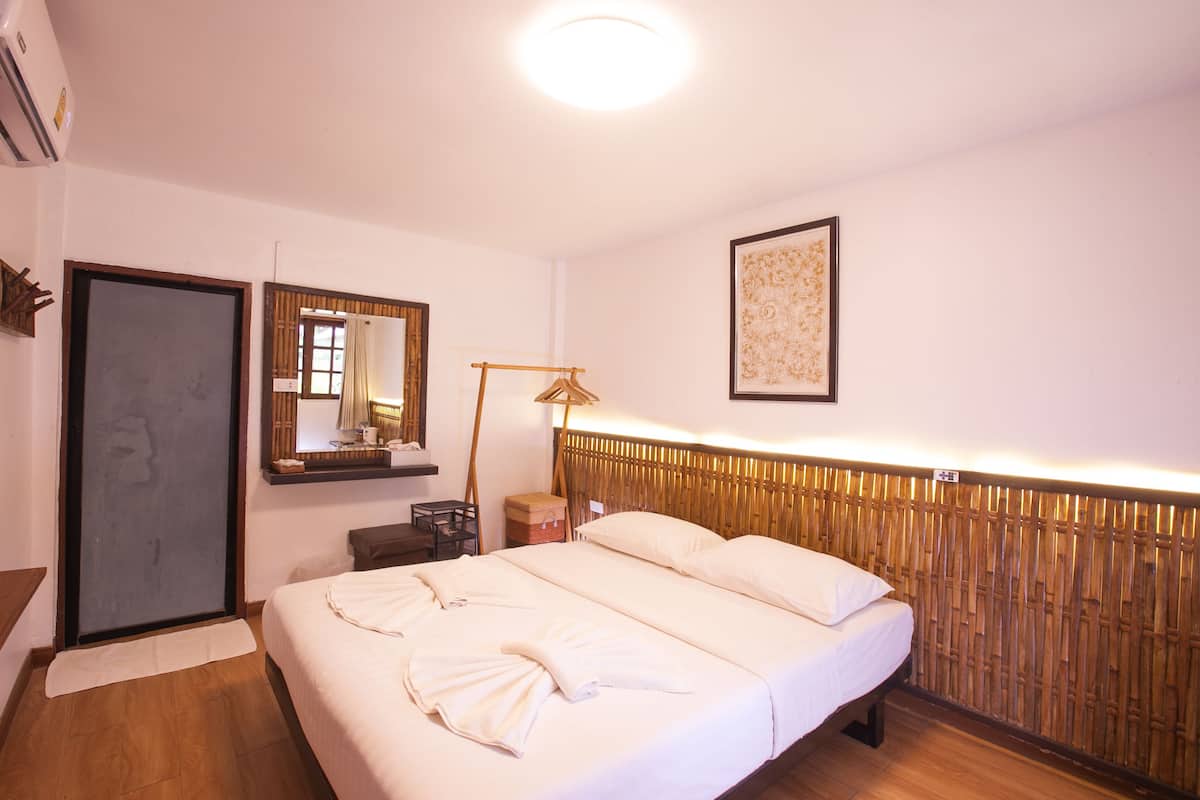 Hotellihuone, jossa on sänky, yöpöytä, lamppu, peili ja seinälle kiinnitetty taideteos.
