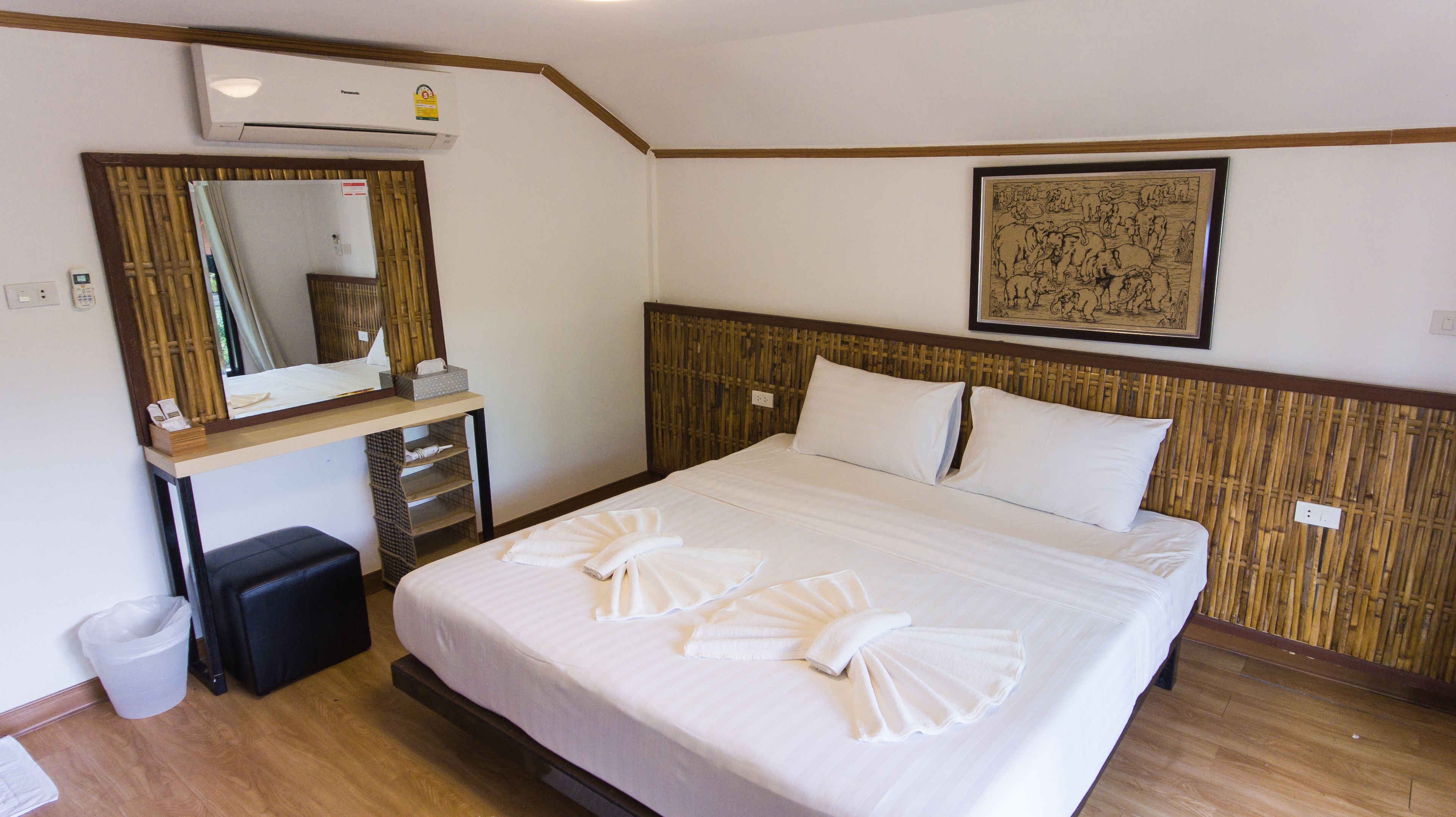 Een hotelkamer met een bed, nachtkastje, spiegel, een inlijsting foto aan de muur, en een prullenbak.