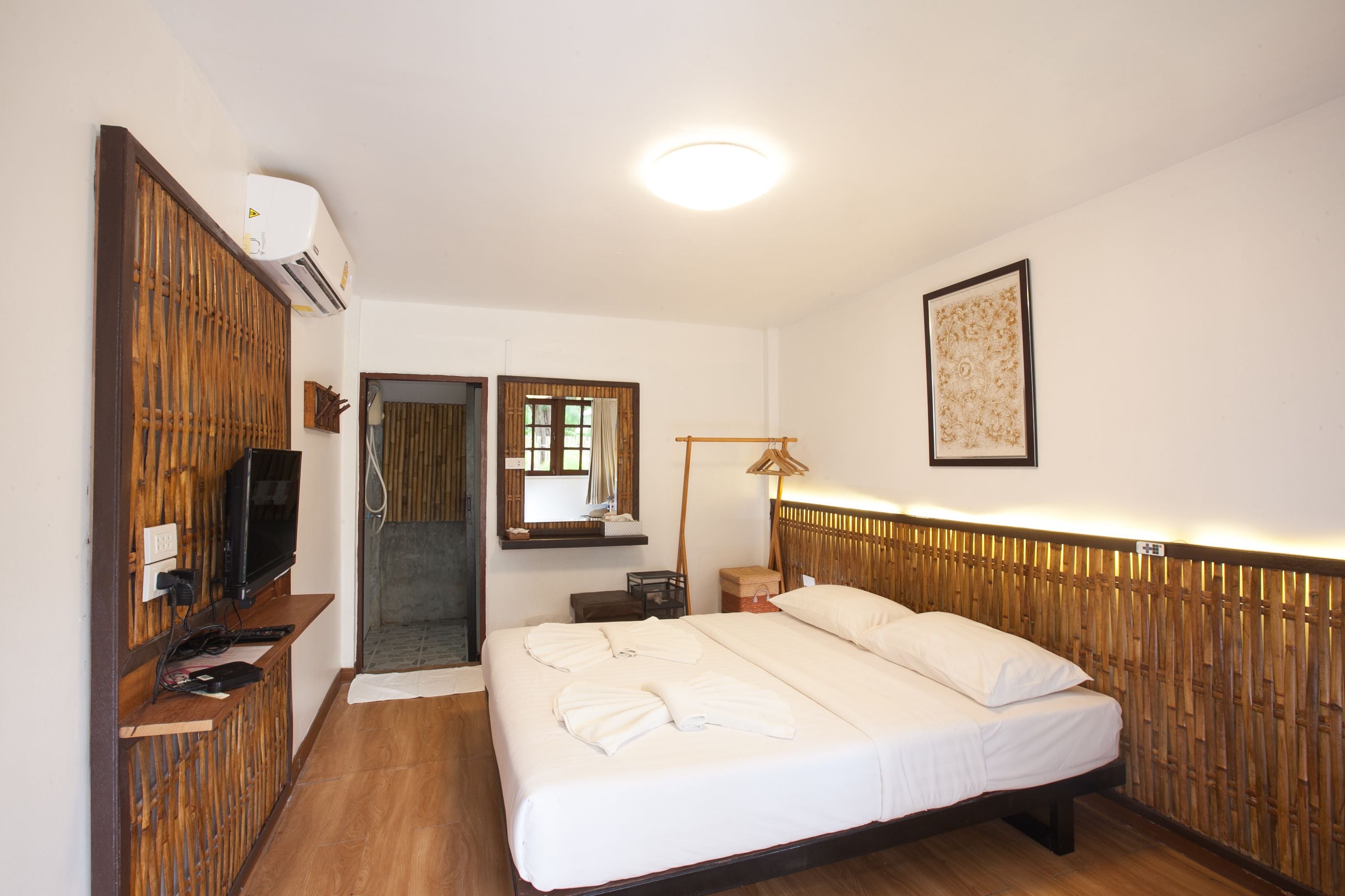 A hotel room with a bed, a television, an air conditioning unit, a mirror, and a framed picture on the wall.