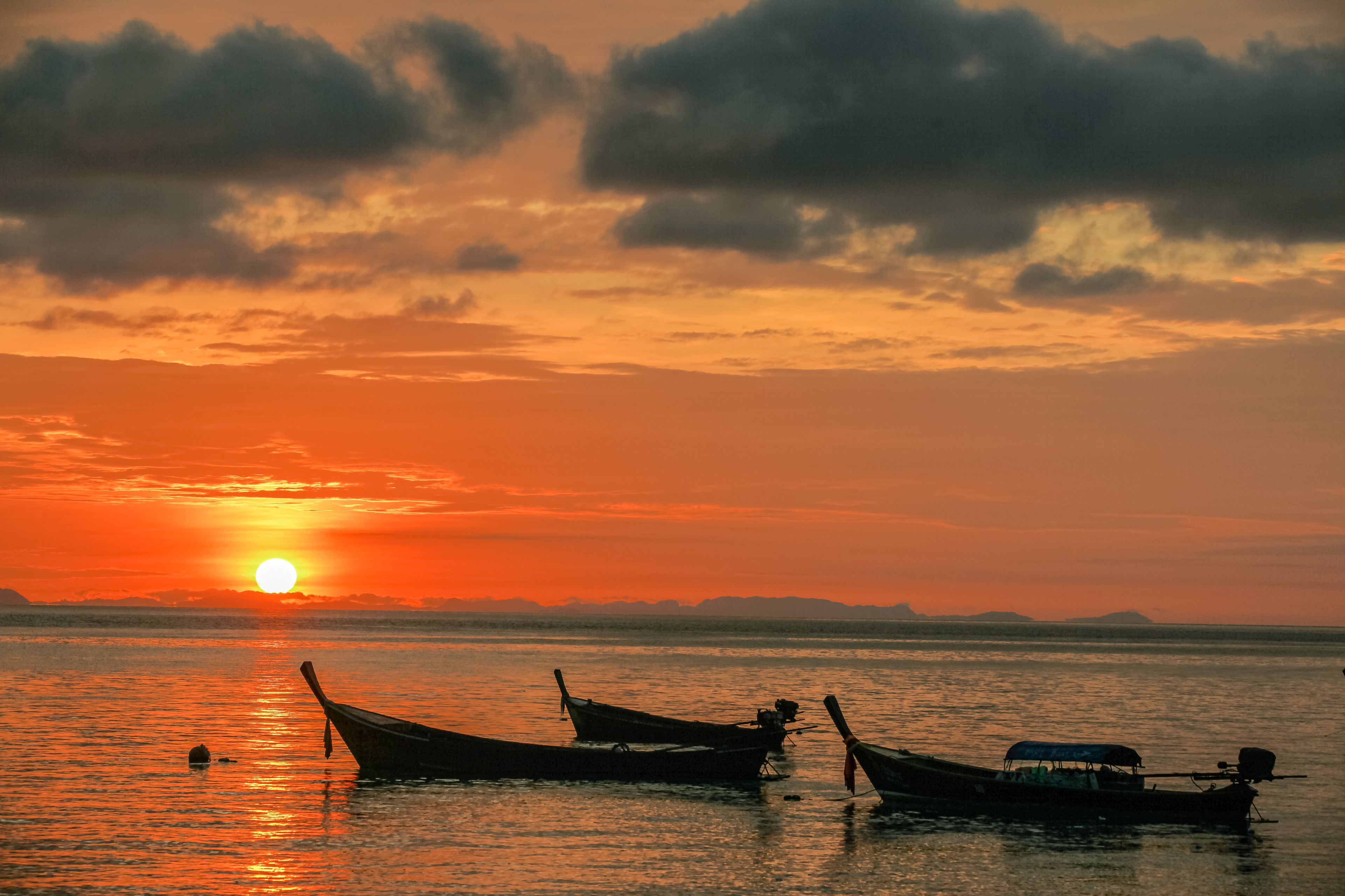 A sunset over a calm body of water with several boats.