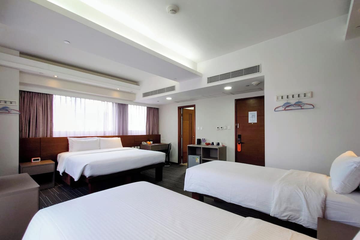 A hotel room with two single beds, a desk, a chair, a wardrobe, and a bathroom door.