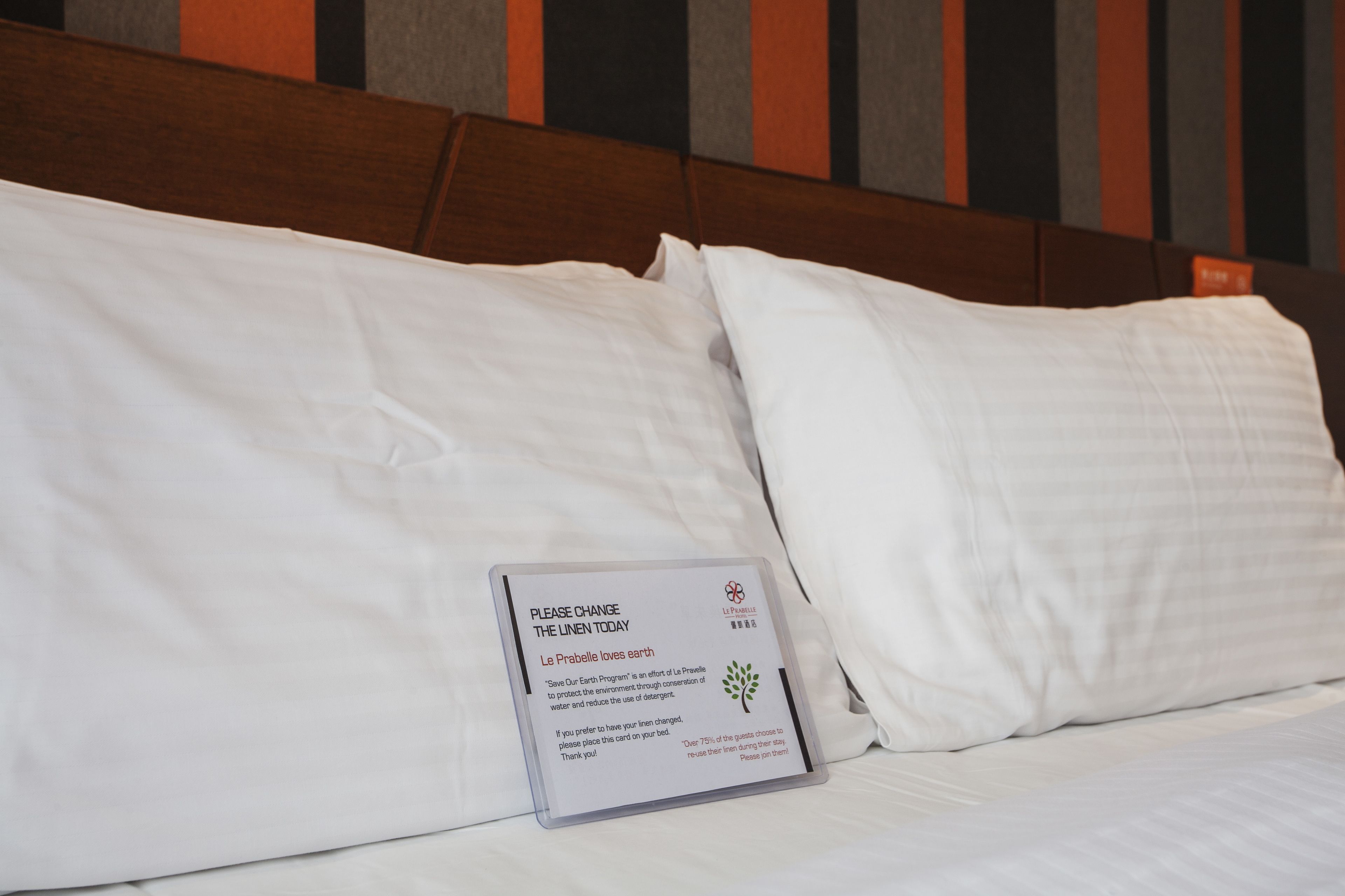A hotel bed with white linens and a card on the pillow requesting guests to change the linen today.