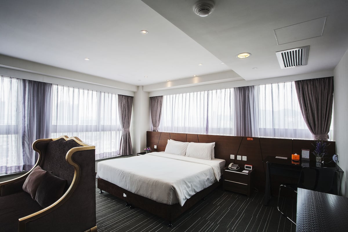 A hotel room with a large bed, a desk, a chair, and a window with curtains.
