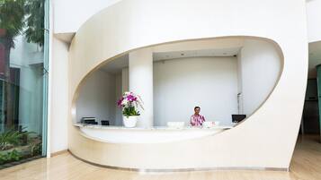 A reception desk with a curved design, a potted plant, and a laptop.