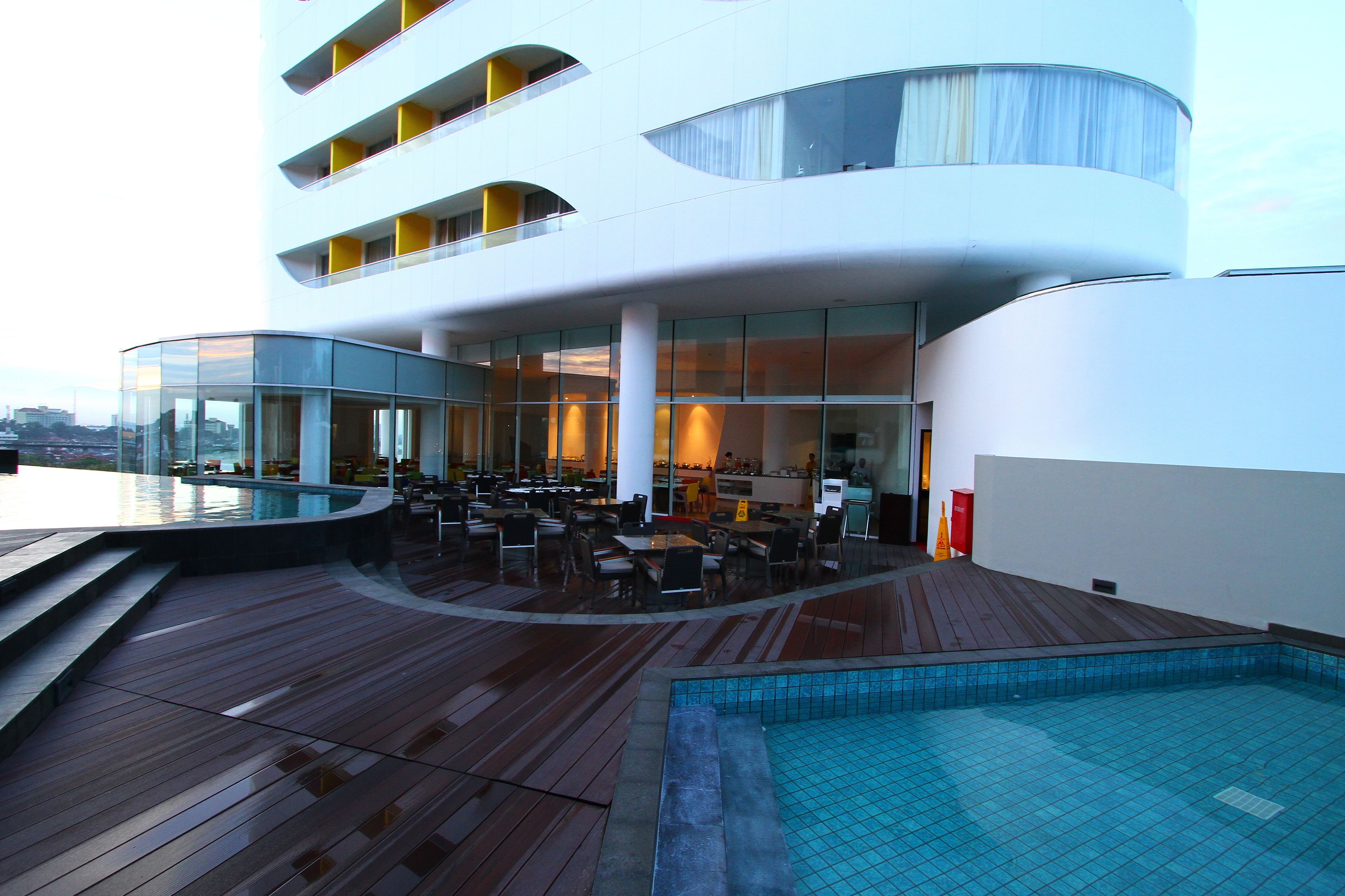 A modern hotel with a rooftop pool area, outdoor dining, and a view of the city.