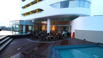 A modern hotel with a rooftop pool area, outdoor dining, and a view of the city.