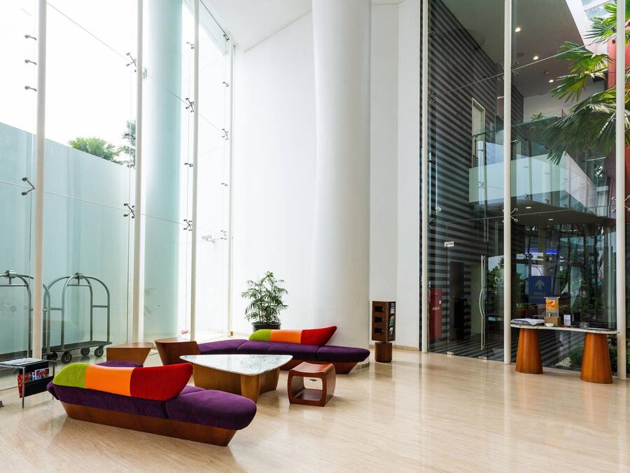 Un lobby moderno con amplios ventanales, una zona de estar con cojines coloridos y un ascensor de vidrio.