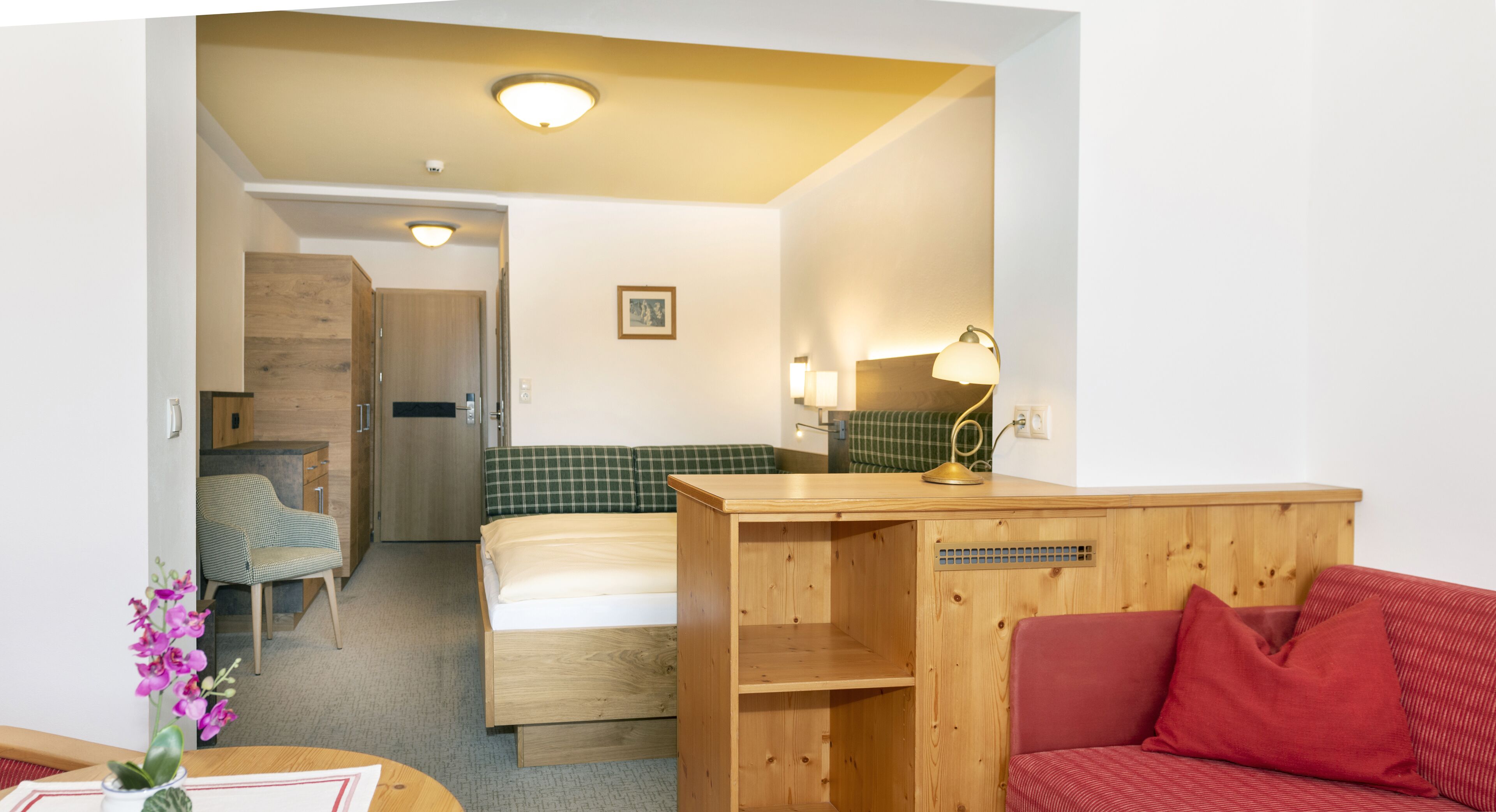 A compact hotel room with a bed, a desk, a chair, and a red sofa.
