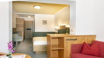 A compact hotel room with a bed, a desk, a chair, and a red sofa.