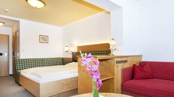 A hotel room with a bed, a red sofa, a desk with a lamp, and a small table with a vase of flowers.