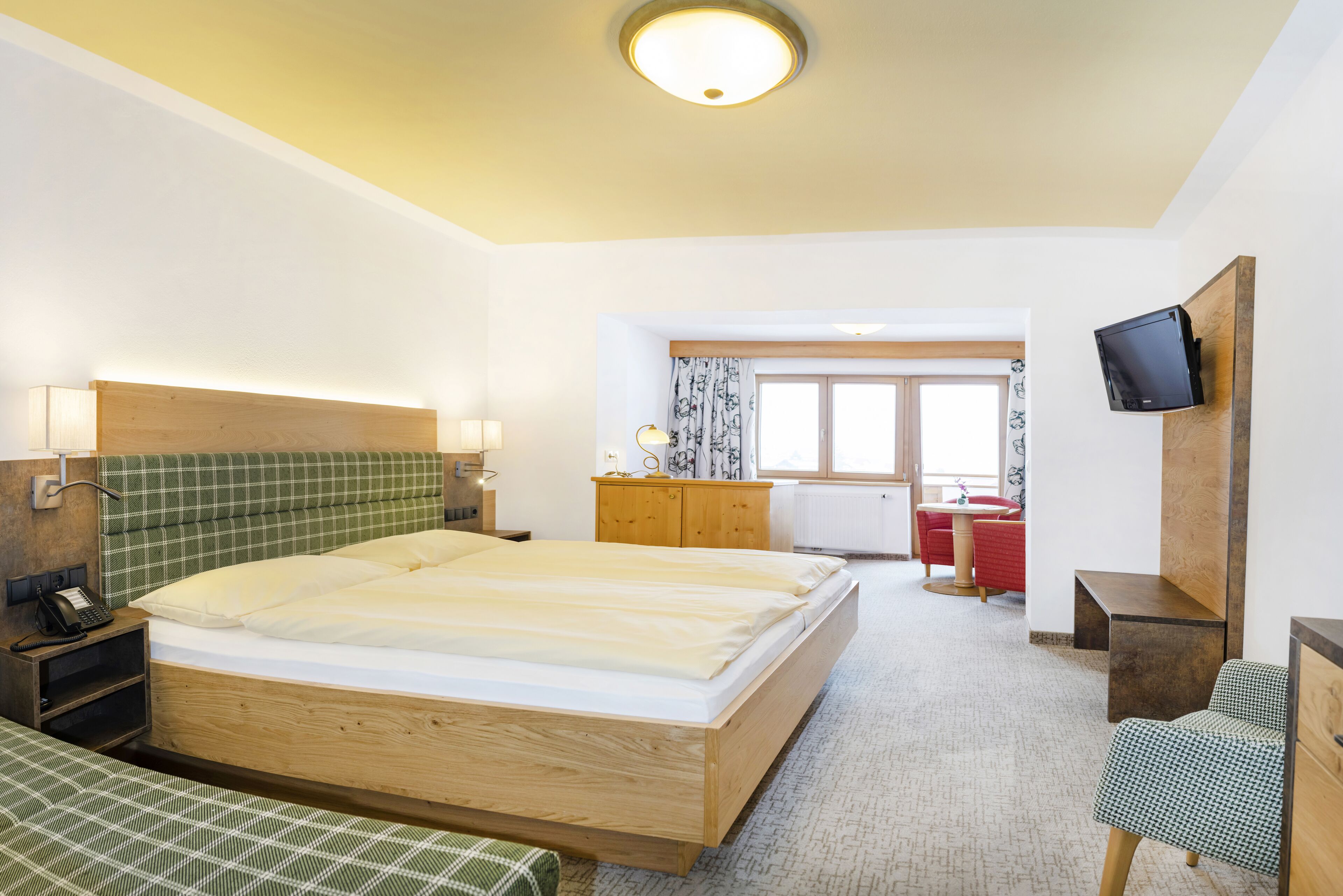 Una habitación de hotel con una cama grande, un escritorio, una silla, un televisor montado en la pared y una ventana con cortinas.
