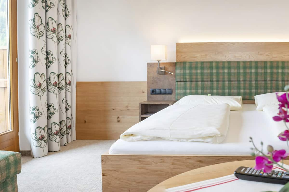 A hotel room with two beds, wooden headboards, bedside lamps, a remote control, and a vase with flowers.