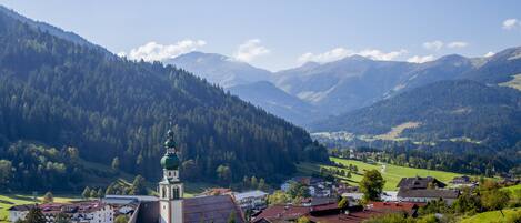 A town with a prominent church featuring a tall tower, surrounded by lush green hills and mountains.
