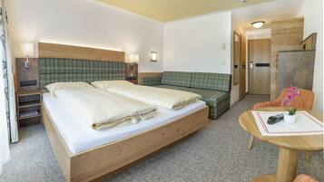 Habitación de hotel con cama de madera, sofá verde a cuadros, una mesita con control remoto y una planta en maceta.