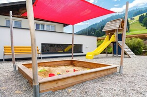 Un parque infantil con un arenero, tobogán amarillo y casita de madera.