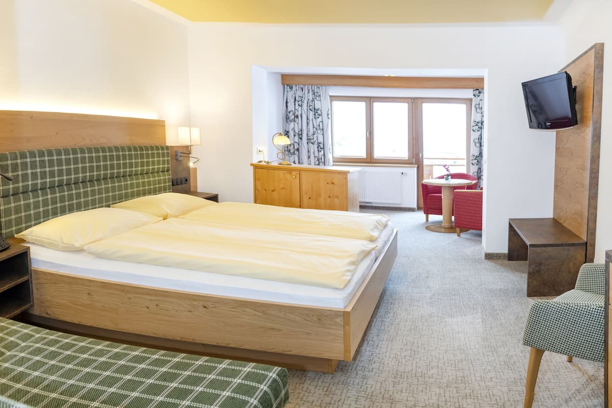 A hotel room with a double bed, a wooden headboard, a desk with a chair, a television mounted on the wall, and a window with curtains.