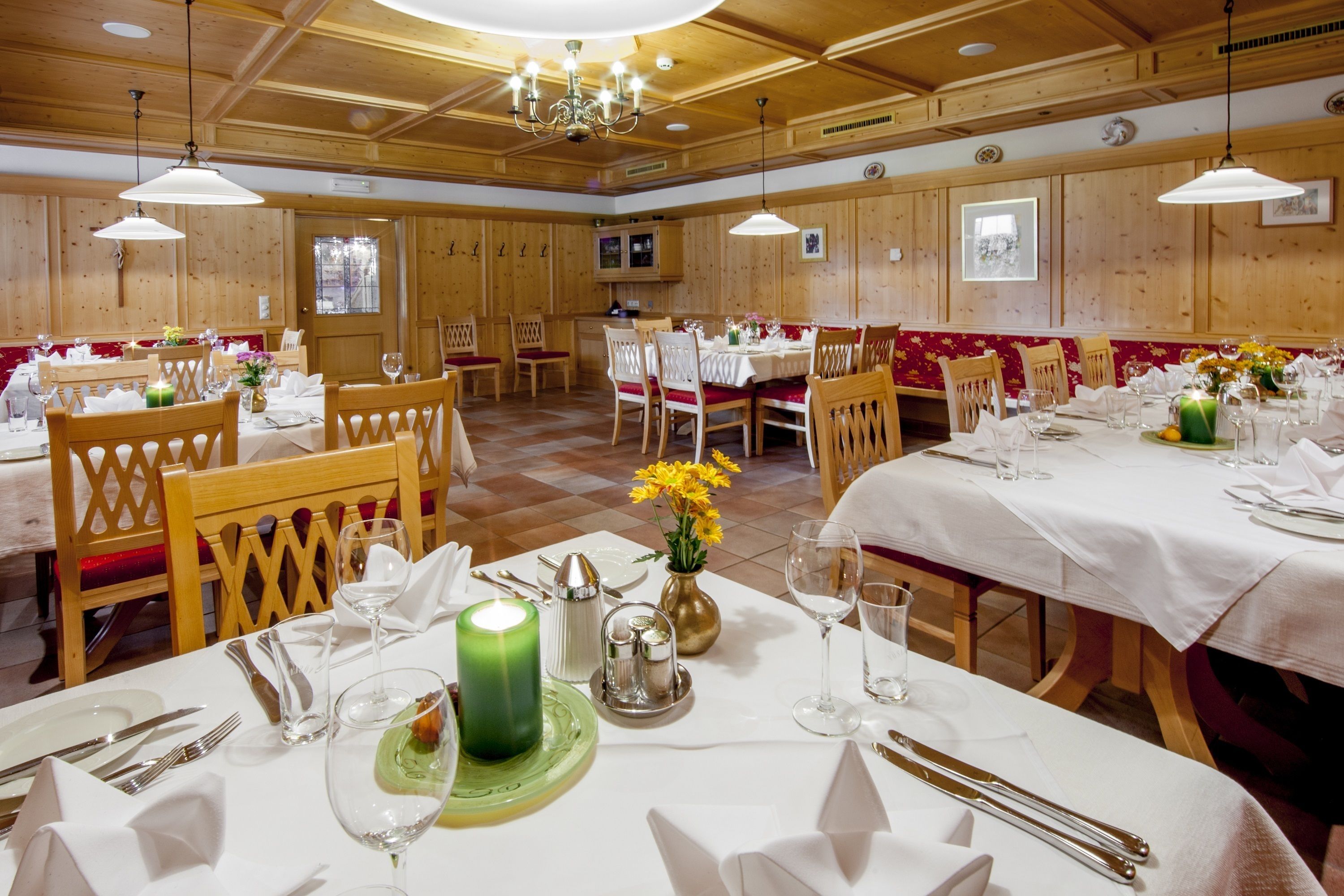Een restaurant met houten lambrisering, witte tafelkleden en keurig gedekte tafels met kaarsen en bloemen.
