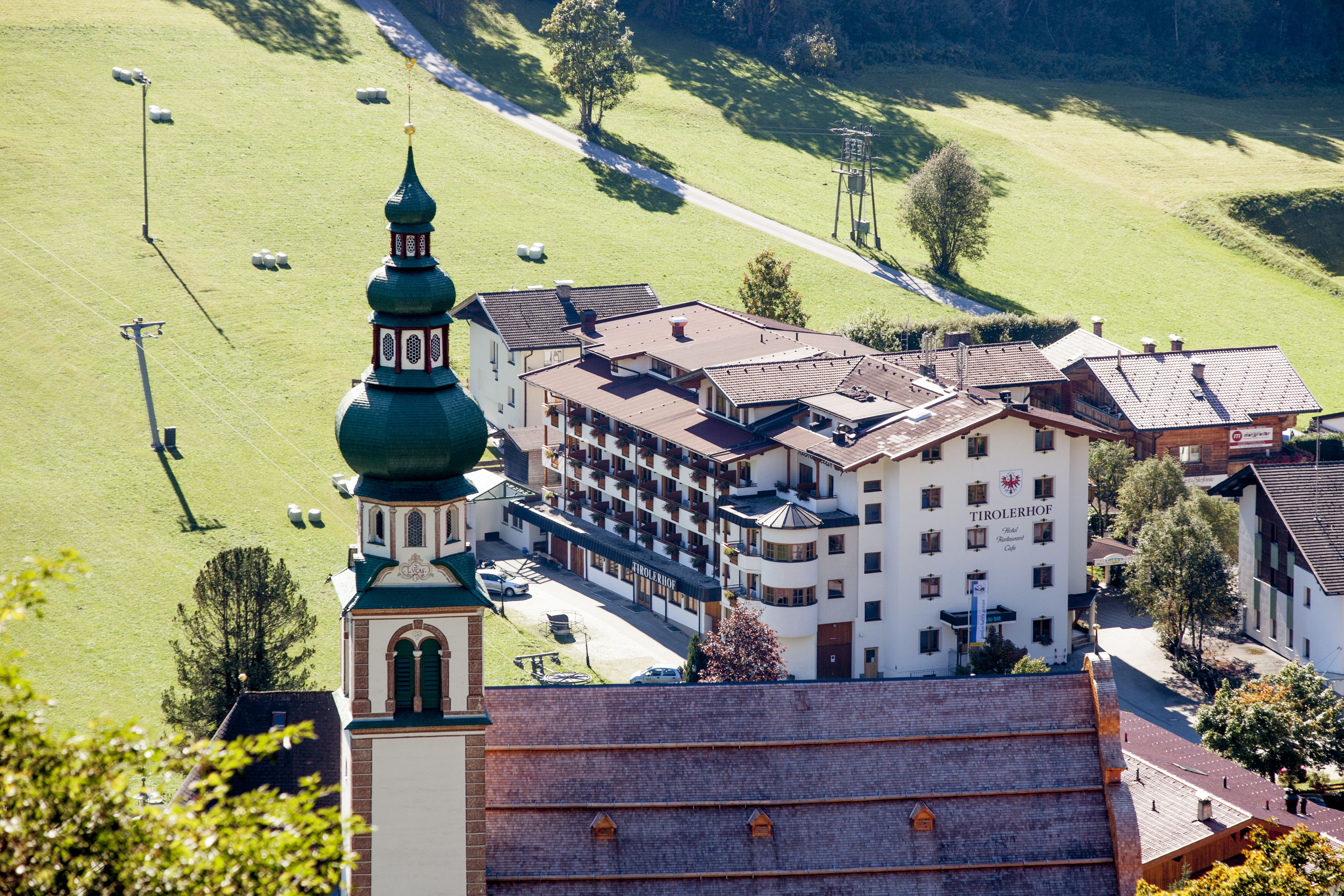 Un hotel con una torre destacada de techo verde, varias edificaciones y un paisaje verde circundante.