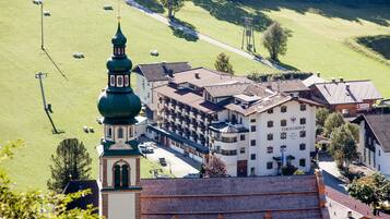 Un hotel con una torre destacada de techo verde, varias edificaciones y un paisaje verde circundante.