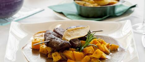 Prato de comida com carne e legumes, um copo de vinho e uma tigela de batatas fritas sobre uma mesa.