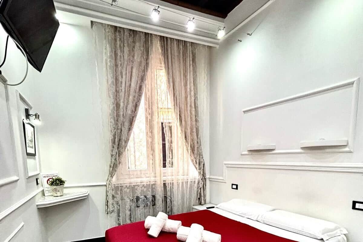 A modern hotel room with a bed, a nightstand, a TV, and a window with curtains.