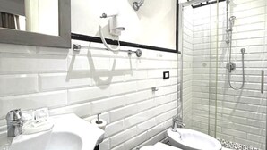 A modern bathroom with a white sink, toilet, and bidet, a shower with glass doors, and a large mirror. - Antica Locanda dell'Orso (Rome)
